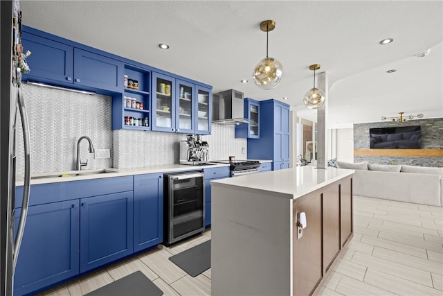 kitchen featuring pendant lighting, a center island, wall chimney range hood, blue cabinets, and wine cooler