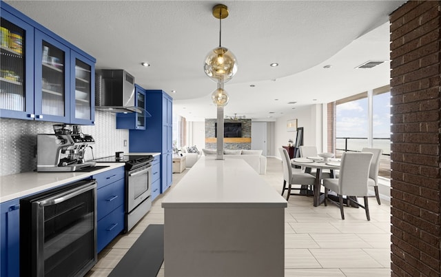 kitchen with decorative backsplash, blue cabinets, beverage cooler, wall chimney range hood, and range