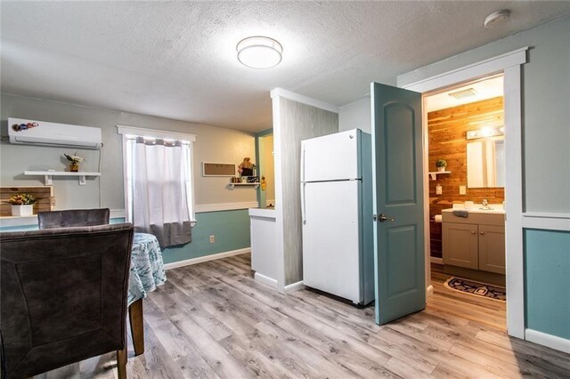 938 E Lakeside Dr, Corpus Christi, TX 78418 - kitchen featuring freestanding refrigerator, a wall mounted air conditioner, light wood finished floors, a textured ceiling, and a sink