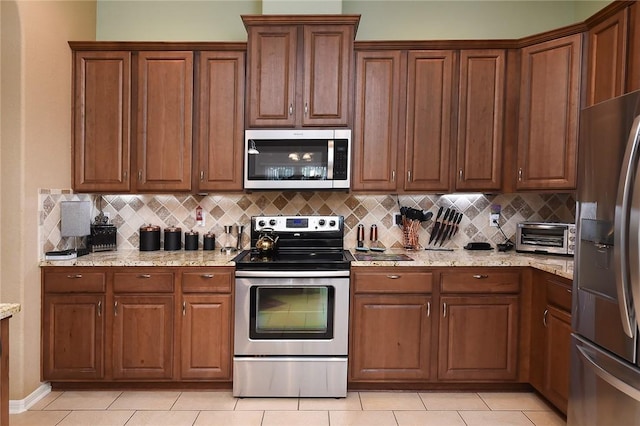 kitchen with tasteful backsplash, light tile patterned flooring, light stone countertops, and appliances with stainless steel finishes