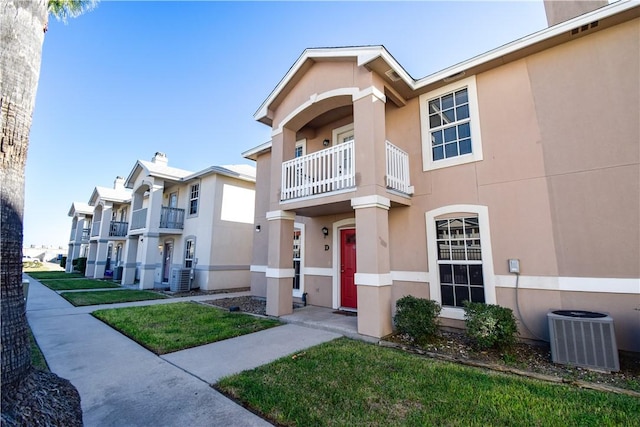 view of front of property with central AC unit, a front yard, a balcony, and stucco siding