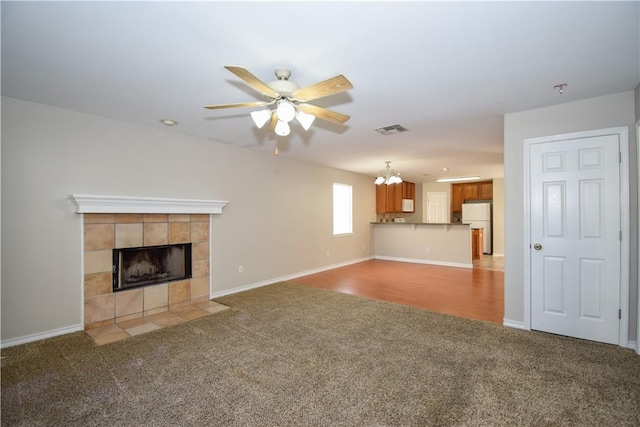 unfurnished living room featuring light carpet, ceiling fan with notable chandelier, a tile fireplace, and visible vents