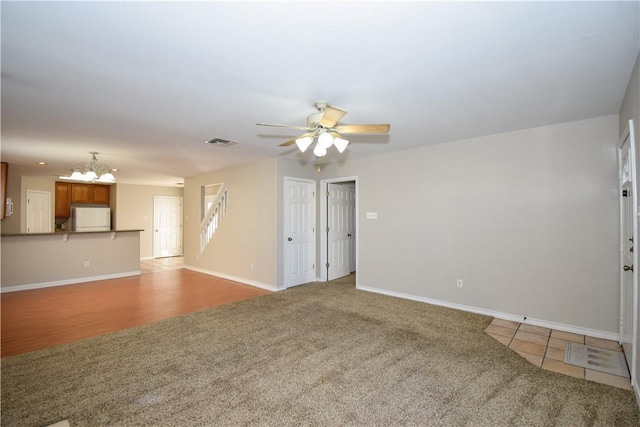 unfurnished living room with light tile patterned floors, baseboards, visible vents, light colored carpet, and ceiling fan with notable chandelier