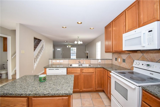 kitchen with white appliances, brown cabinetry, a peninsula, a sink, and backsplash