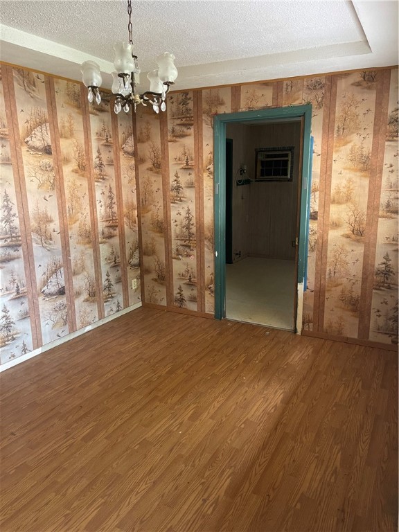 empty room featuring wood-type flooring, a textured ceiling, and an inviting chandelier