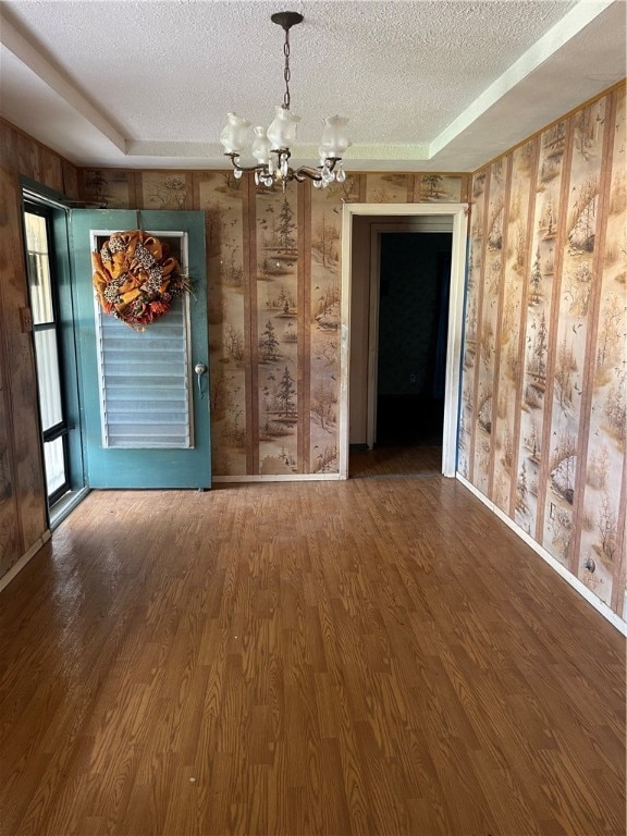 empty room with hardwood / wood-style floors, a textured ceiling, a tray ceiling, and an inviting chandelier