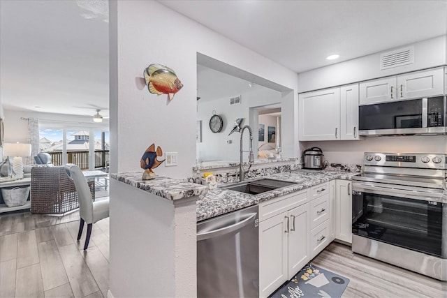 kitchen featuring stainless steel appliances, sink, light stone counters, kitchen peninsula, and white cabinets