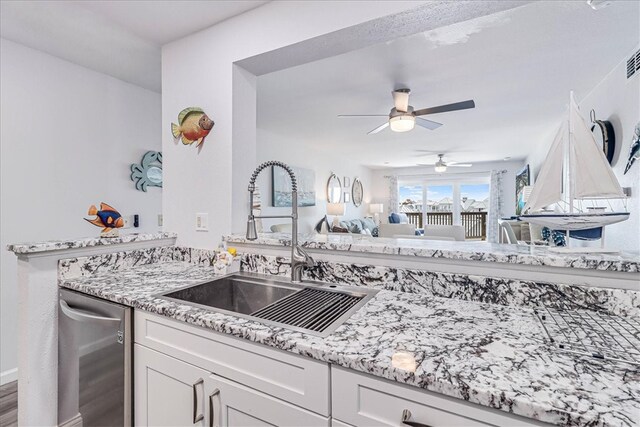 kitchen with light stone counters, sink, stainless steel dishwasher, ceiling fan, and white cabinetry