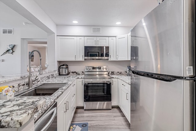 kitchen featuring stainless steel appliances, white cabinetry, sink, light stone counters, and light hardwood / wood-style flooring