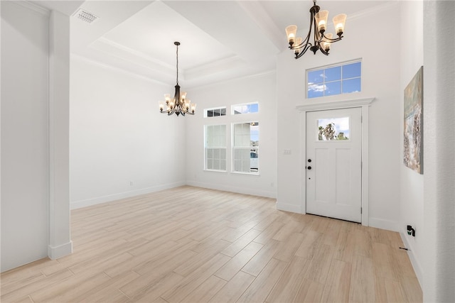 foyer entrance with light wood-type flooring, a notable chandelier, crown molding, and a raised ceiling