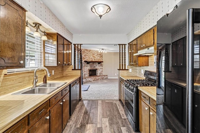 11129 Mulholland Dr, Corpus Christi, TX 78410 - kitchen with appliances with stainless steel finishes, wallpapered walls, under cabinet range hood, dark wood-style flooring, and a brick fireplace