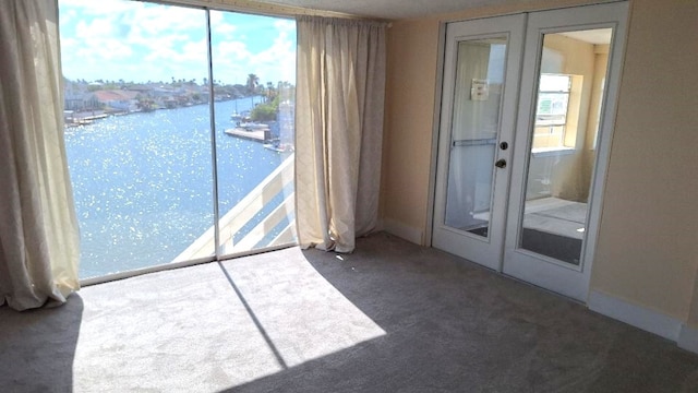 carpeted empty room with plenty of natural light, french doors, and a water view