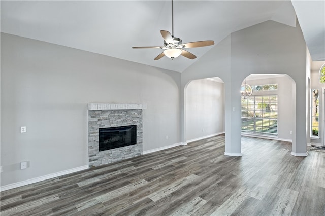 unfurnished living room with ceiling fan with notable chandelier, dark hardwood / wood-style flooring, high vaulted ceiling, and a stone fireplace