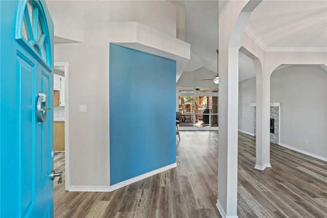 foyer with ornamental molding, a stone fireplace, ceiling fan, and dark wood-type flooring