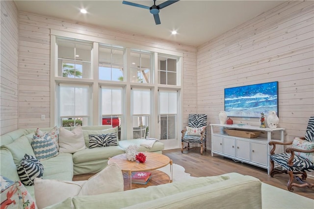 living room with ceiling fan, light wood-type flooring, a high ceiling, and wood walls