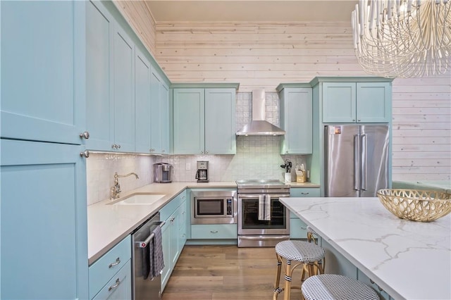 kitchen with appliances with stainless steel finishes, decorative light fixtures, sink, hardwood / wood-style flooring, and wall chimney range hood