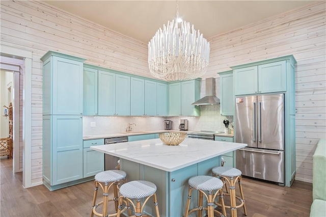 kitchen featuring appliances with stainless steel finishes, pendant lighting, a center island, an inviting chandelier, and wall chimney exhaust hood