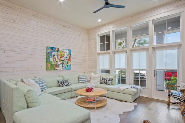 living room with a high ceiling, hardwood / wood-style floors, ceiling fan, and wood walls