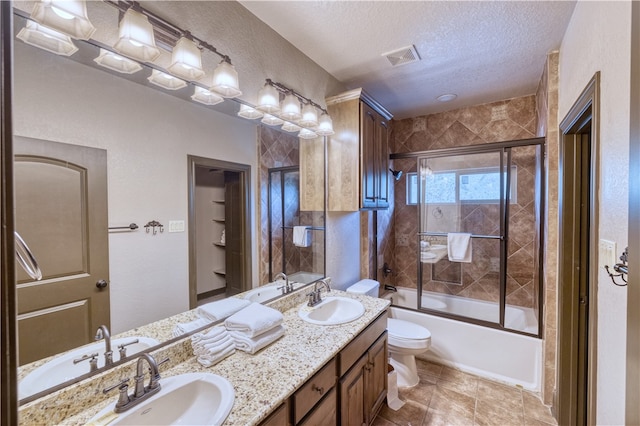 full bathroom with toilet, bath / shower combo with glass door, tile patterned flooring, a textured ceiling, and vanity