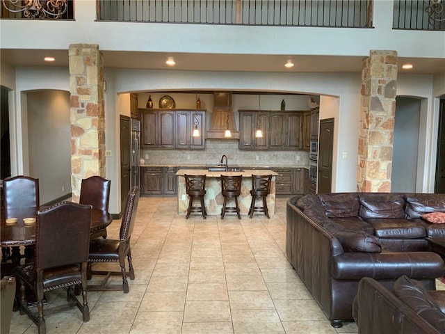 tiled living room featuring decorative columns, sink, and a towering ceiling