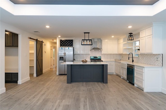 kitchen with appliances with stainless steel finishes, a center island, decorative light fixtures, a barn door, and wall chimney exhaust hood