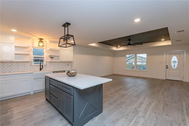 kitchen with white cabinetry, sink, hanging light fixtures, a raised ceiling, and light hardwood / wood-style flooring