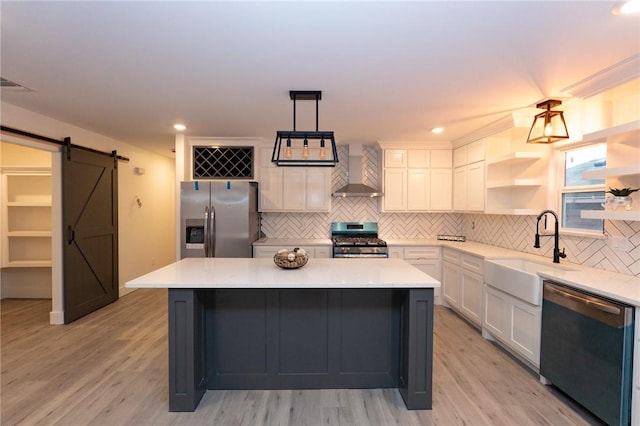 kitchen featuring sink, decorative light fixtures, appliances with stainless steel finishes, a barn door, and wall chimney range hood