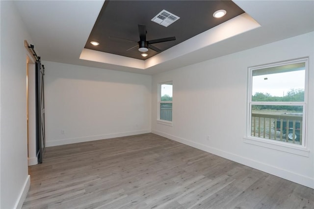 empty room featuring ceiling fan, a barn door, a raised ceiling, and light wood-type flooring