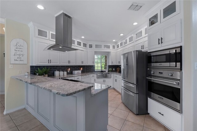 kitchen featuring white cabinetry, kitchen peninsula, light stone counters, appliances with stainless steel finishes, and island exhaust hood