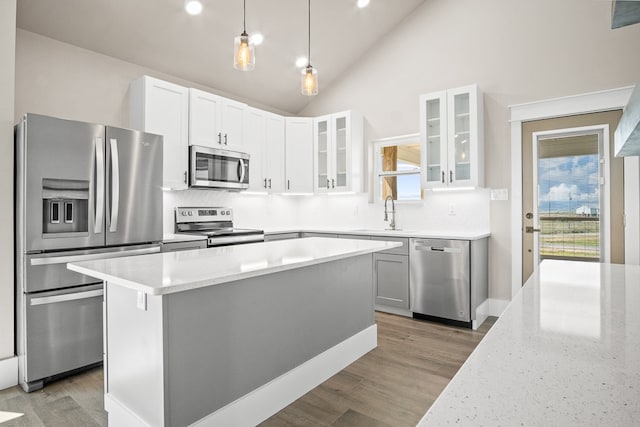 kitchen featuring hardwood / wood-style flooring, white cabinetry, appliances with stainless steel finishes, decorative light fixtures, and a kitchen island