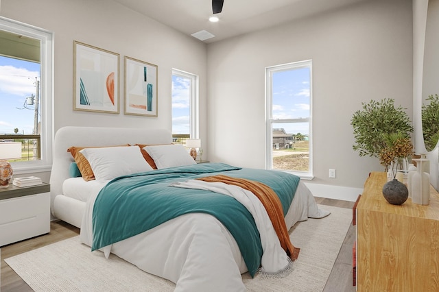 bedroom with ceiling fan, wood-type flooring, and multiple windows