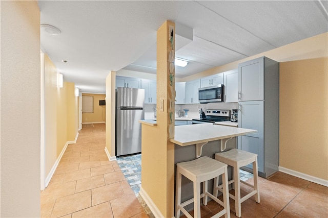 kitchen with a kitchen breakfast bar, light tile patterned floors, kitchen peninsula, and appliances with stainless steel finishes