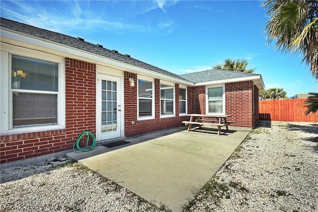 exterior space with roof with shingles, fence, and brick siding