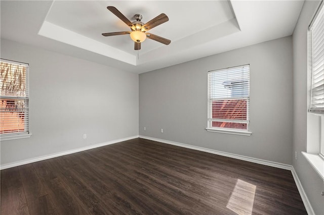 spare room with dark wood-style floors, baseboards, a tray ceiling, and ceiling fan