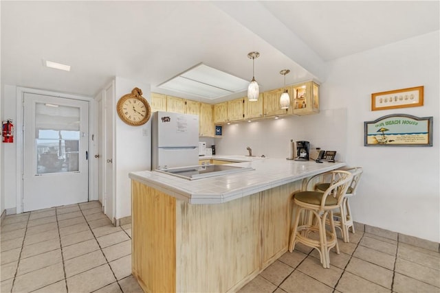 kitchen with kitchen peninsula, white fridge, decorative light fixtures, a kitchen bar, and light brown cabinetry