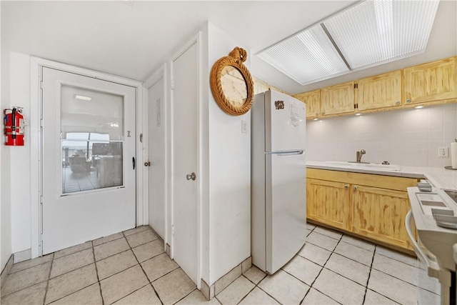 kitchen featuring sink, light brown cabinets, backsplash, white fridge, and range