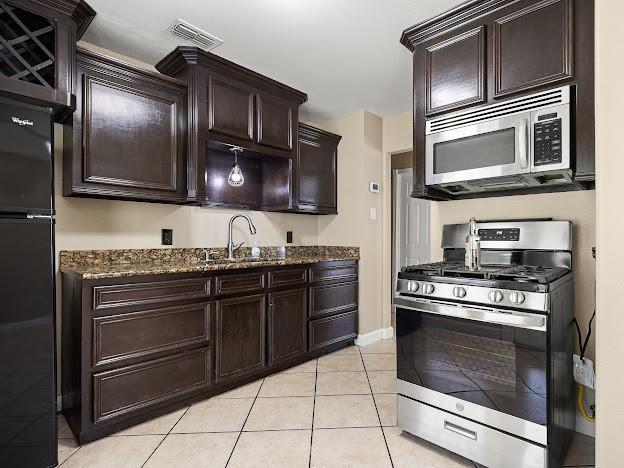 4546 Prescott St, Corpus Christi, TX 78416 - kitchen featuring stainless steel appliances, dark stone counters, light tile patterned floors, and dark brown cabinets