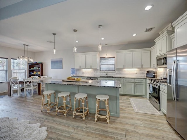 kitchen with appliances with stainless steel finishes, a sink, backsplash, stone countertops, and a center island