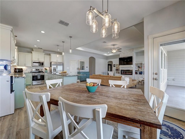 dining room with a ceiling fan, light wood finished floors, arched walkways, recessed lighting, and a fireplace