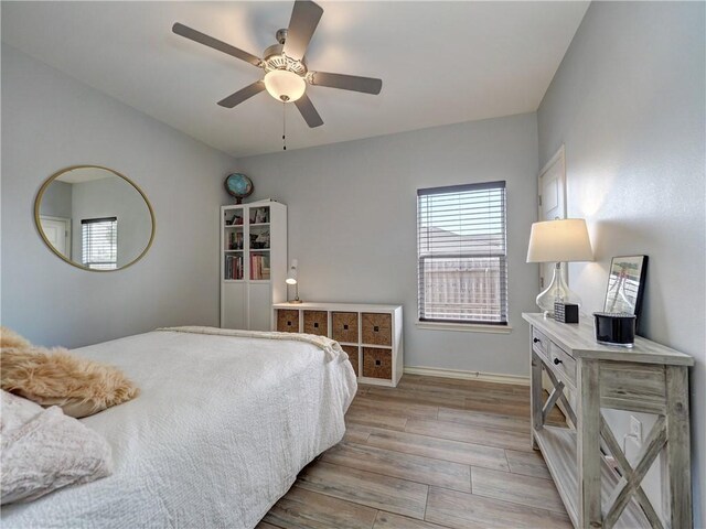 bedroom with light wood-style flooring, multiple windows, baseboards, and ceiling fan