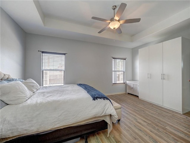 bedroom with a tray ceiling, light wood-style floors, ceiling fan, and baseboards