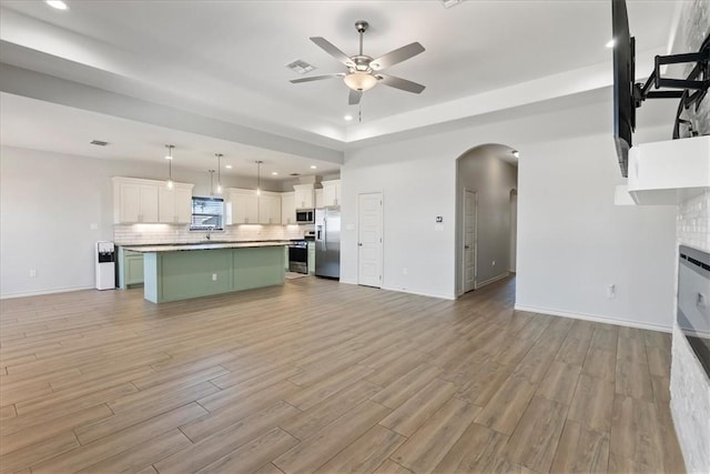 15101 Tesoro Dr, Corpus Christi, TX 78418 - unfurnished living room with ceiling fan, arched walkways, light wood finished floors, recessed lighting, and a tray ceiling