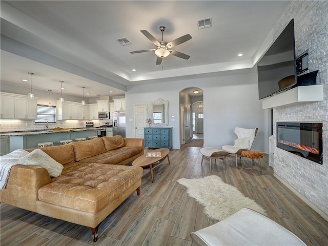 living room with ceiling fan, wood finished floors, arched walkways, recessed lighting, and a glass covered fireplace