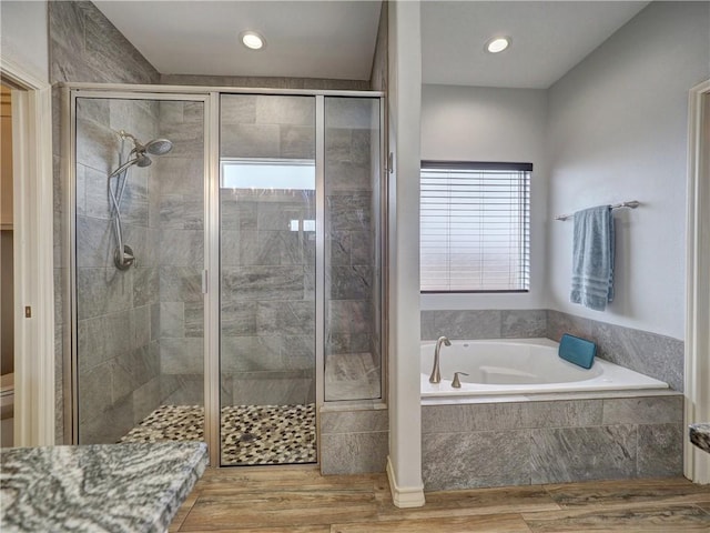 bathroom with a stall shower, wood finished floors, a bath, recessed lighting, and toilet