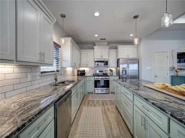 kitchen featuring stainless steel appliances, a sink, dark stone counters, tasteful backsplash, and light wood-style flooring