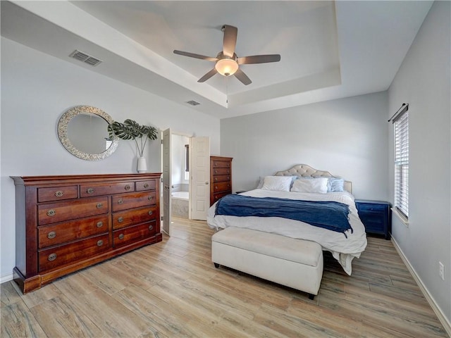 bedroom featuring a tray ceiling, light wood-style flooring, baseboards, and a ceiling fan