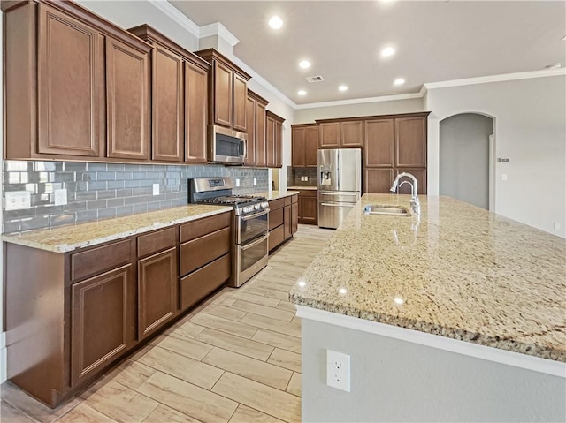 kitchen featuring backsplash, a large island with sink, sink, light stone countertops, and stainless steel appliances