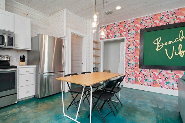 kitchen with wooden walls, appliances with stainless steel finishes, decorative light fixtures, and white cabinets