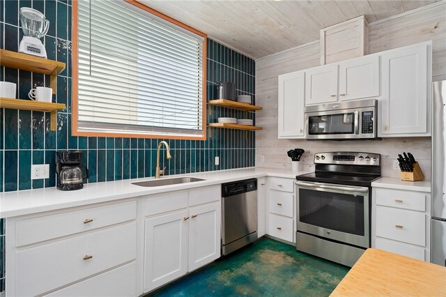 kitchen featuring stainless steel appliances, white cabinets, wood walls, sink, and backsplash