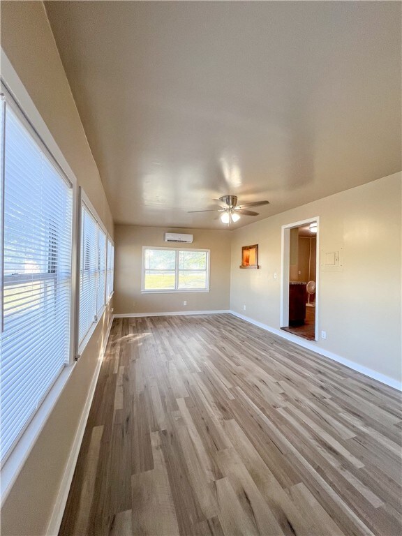 empty room featuring a wall mounted AC, light hardwood / wood-style flooring, and ceiling fan